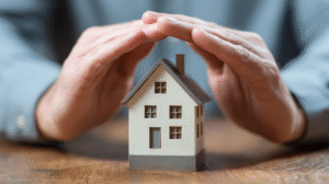 Una persona cubre una casa en miniatura con las manos, simbolizando un seguro de hogar